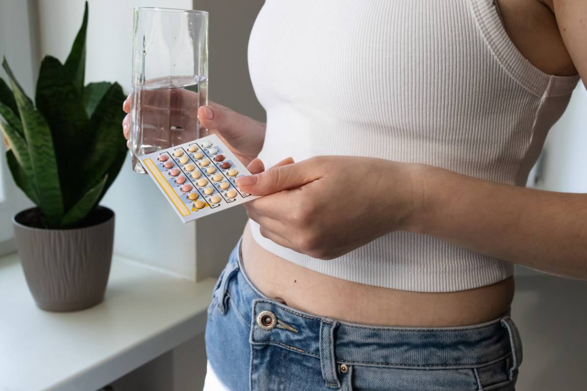 Woman taking oral contraceptive, holding birth control pills and glass of water.