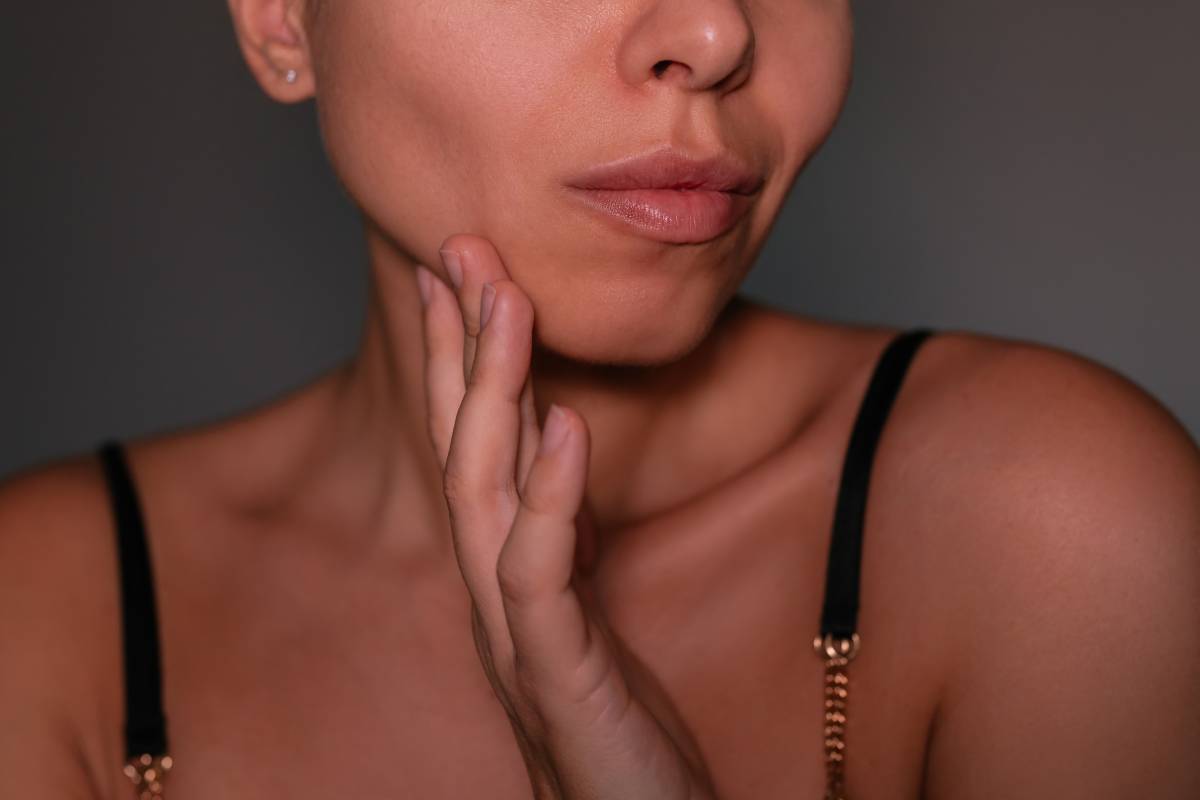 Young woman touching her cheek, showing defined jawline and buccal area. Concept of buccal fat removal, face contouring